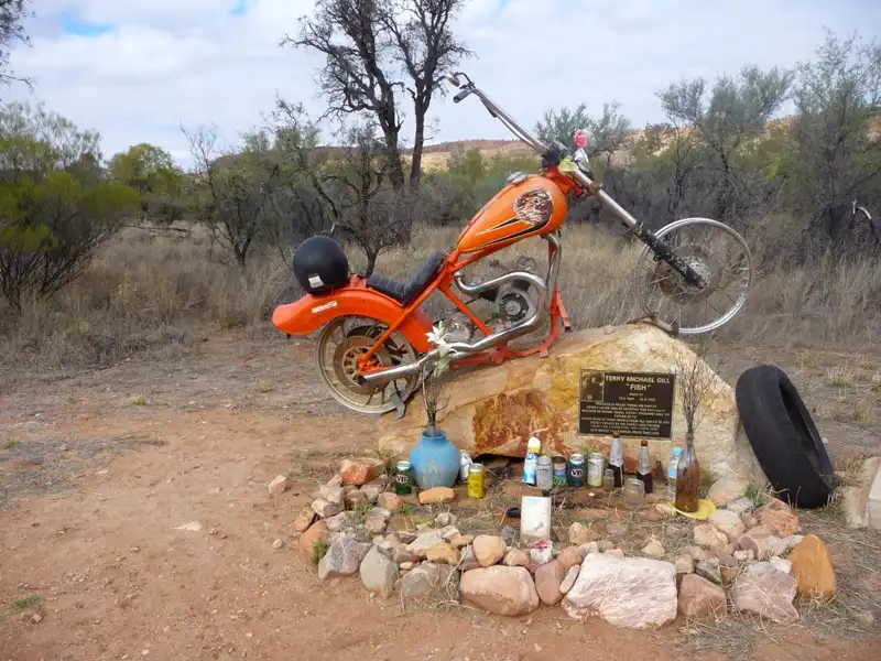 Roadside memorial on the Ross Highway with crosses, flowers, and beer bottles honouring a motorbike rider.