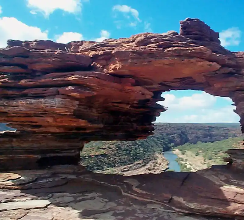 A natural rock arch formation frames a scenic view of a winding river and green landscape under a bright blue sky, reminiscent of the pristine beauty found along the Ningaloo Coast.
