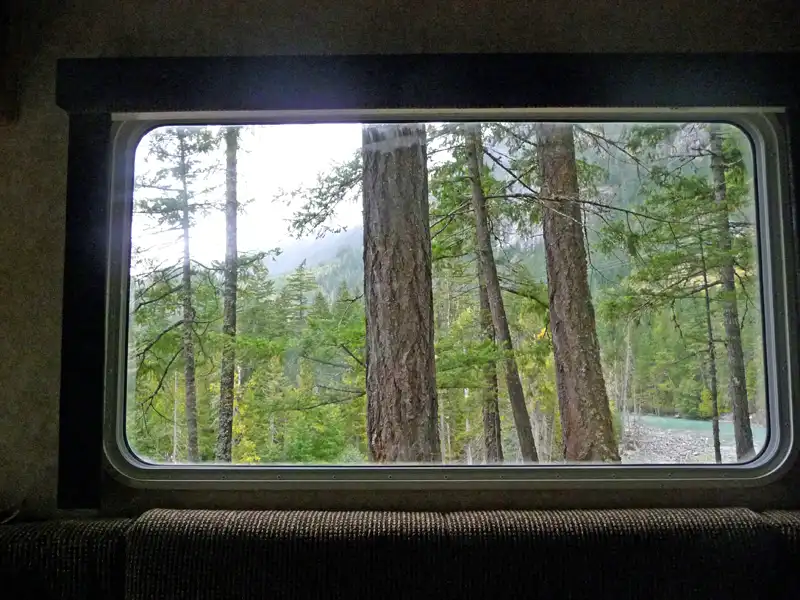 Cosy RV parked in a forest near Whistler, surrounded by tall trees, with a peaceful outdoor setting and a home-cooked meal enjoyed with a bottle of red wine.