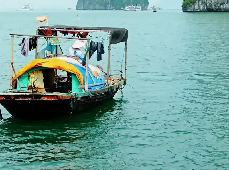 Small fishing boat and floating village in Ha Long Bay with limestone karst islands in the background, Vietnam.