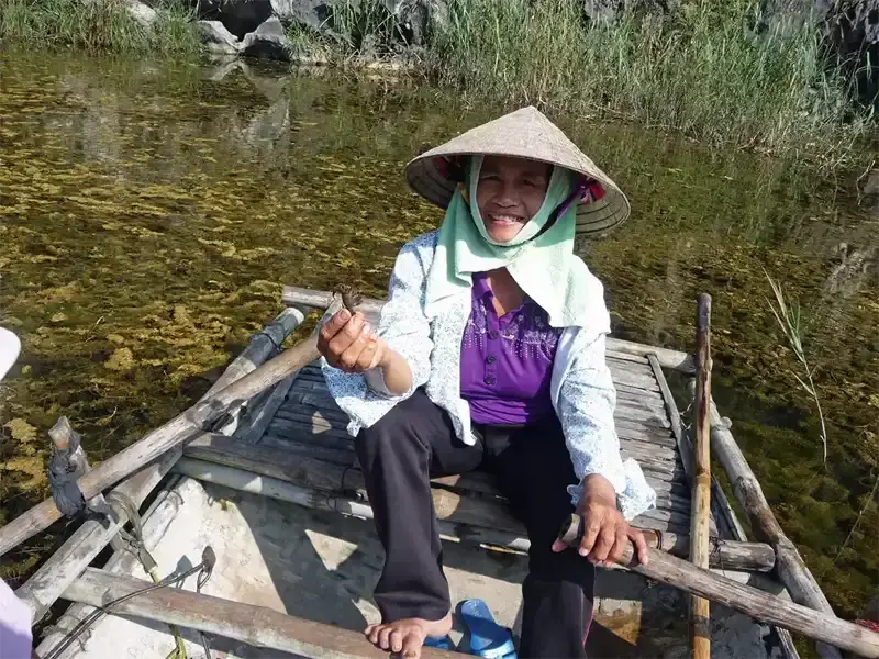 Smiling Vietnamese woman rowing a boat in Ninh Binh, Vietnam